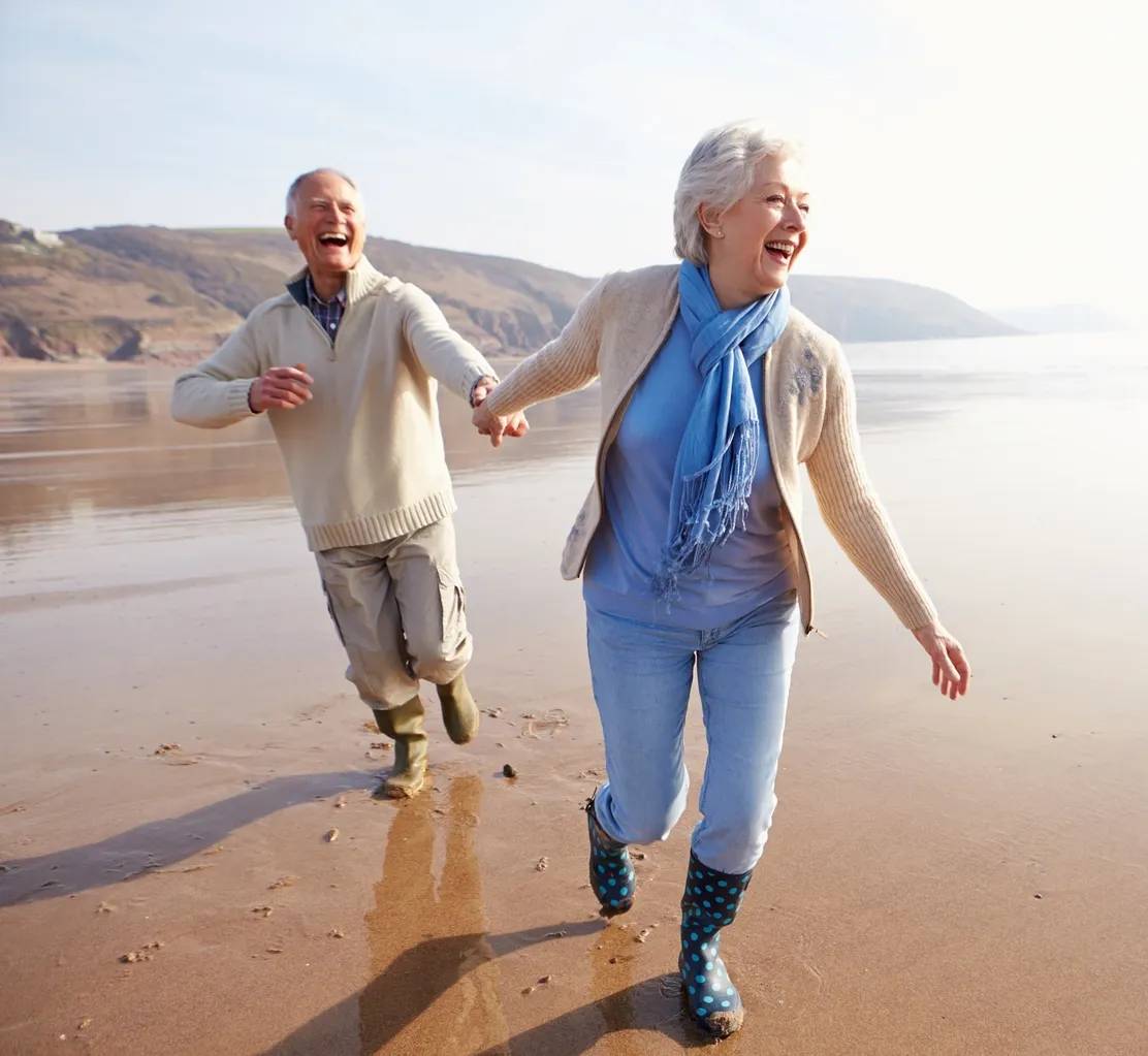 A man and woman holding hands while walking on the beach.